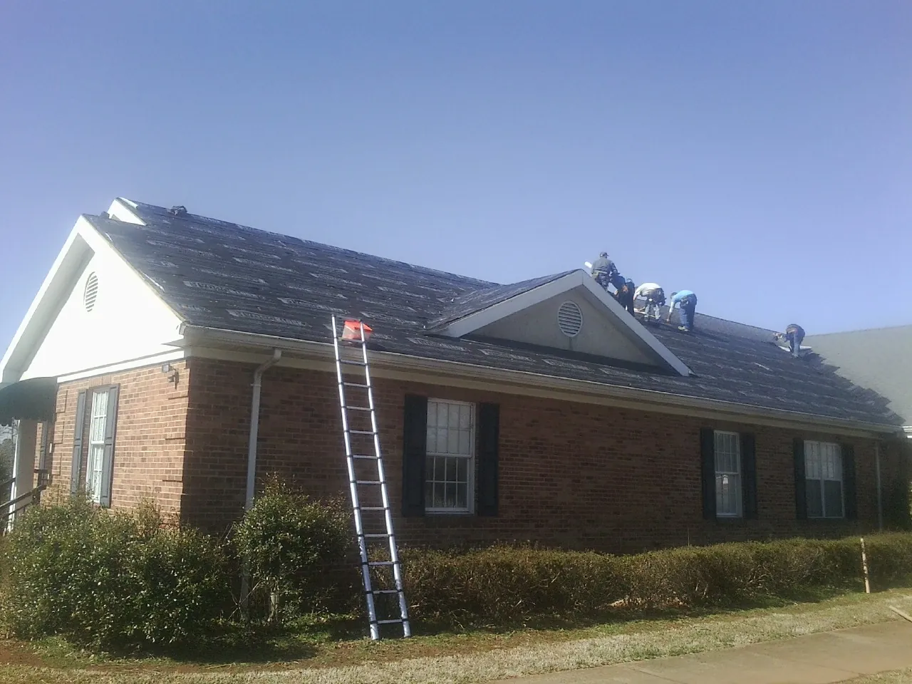 Crew tearing shingles off a brick ranch roof with a ladder set — Metal Roof Repair work by our crew in Speer