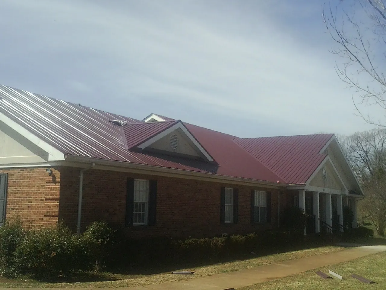 Red metal roof with gabled entries on a long brick building, from a Hail Damage Roof Repair job in Speer